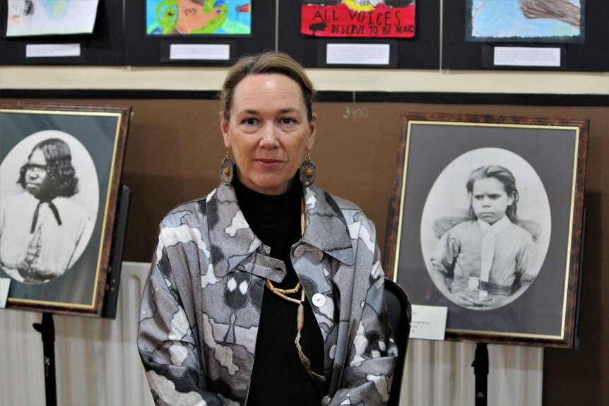 A woman sits between two portraits of Aboriginal children 