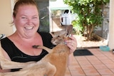 A woman in a black singlet smiles at the camera holding a young kangaroo.