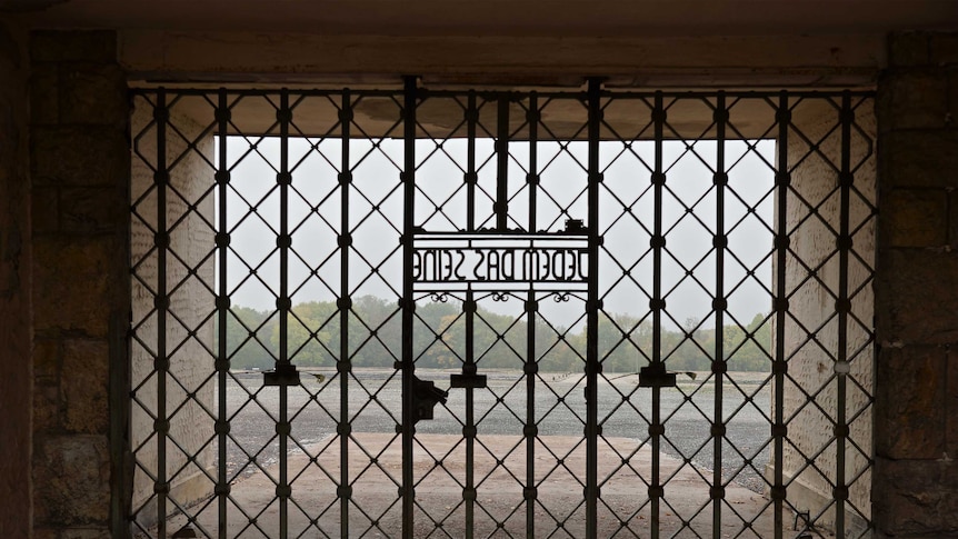 A view of an open field that used to be a concentration camp, through gates that feature the motto "Jedem das Seine".
