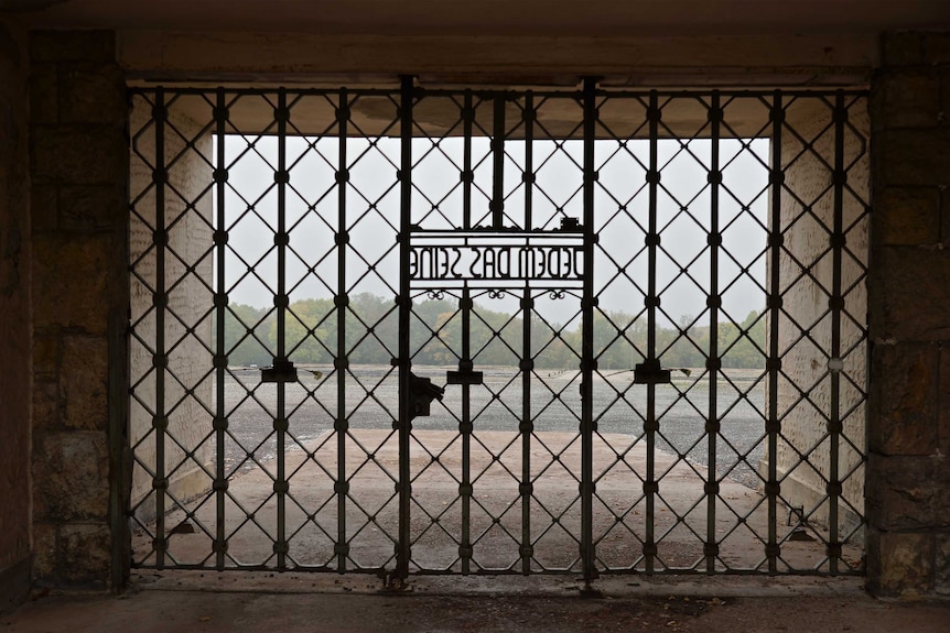 A view of an open field that used to be a concentration camp, through gates that feature the motto "Jedem das Seine".