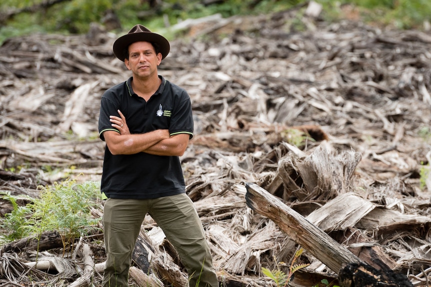 Man with a hat stands in front of logged wood 