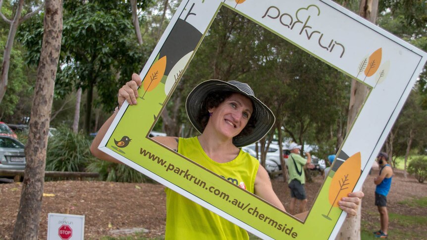 Ada Macey smiles while holding a cardboard parkrun Chermside frame