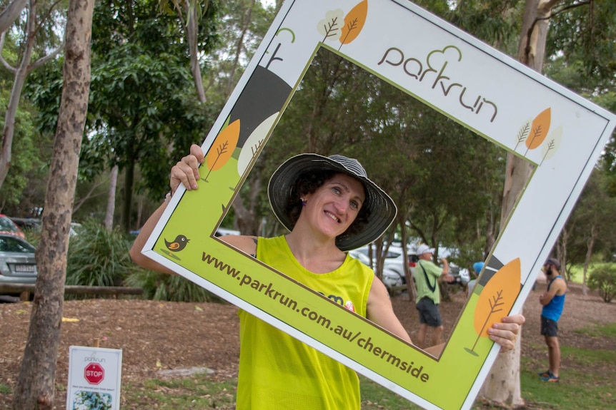 Ada Macey smiles while holding a cardboard parkrun Chermside frame