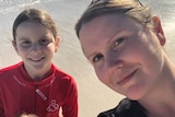 A mum and her two daughters smiling for a selfie photo on the beach.