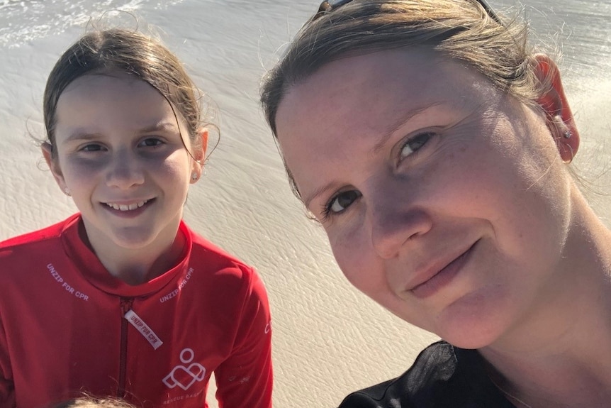 A mum and her two daughters smiling for a selfie photo on the beach.