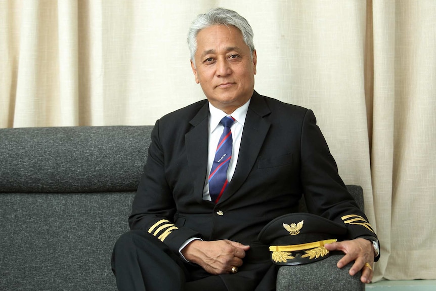 A grey-haired man in a pilot's uniform looks at the camera.