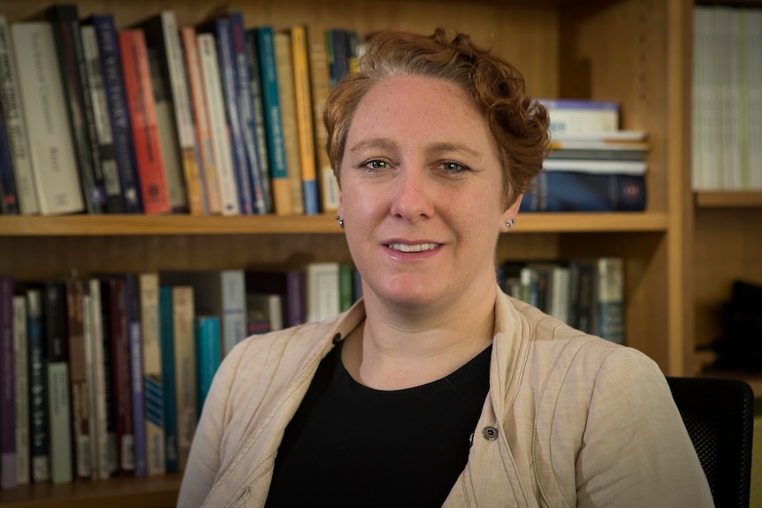 A photo of a woman with short hair in front of a bookshelf.