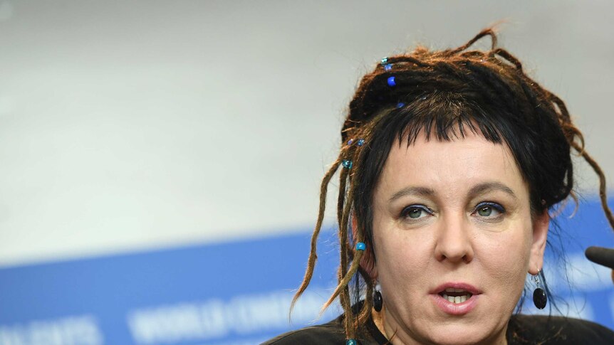 A close up of Olga Tokarczuk, with dreads and blue beads in her hair, talking at a panel
