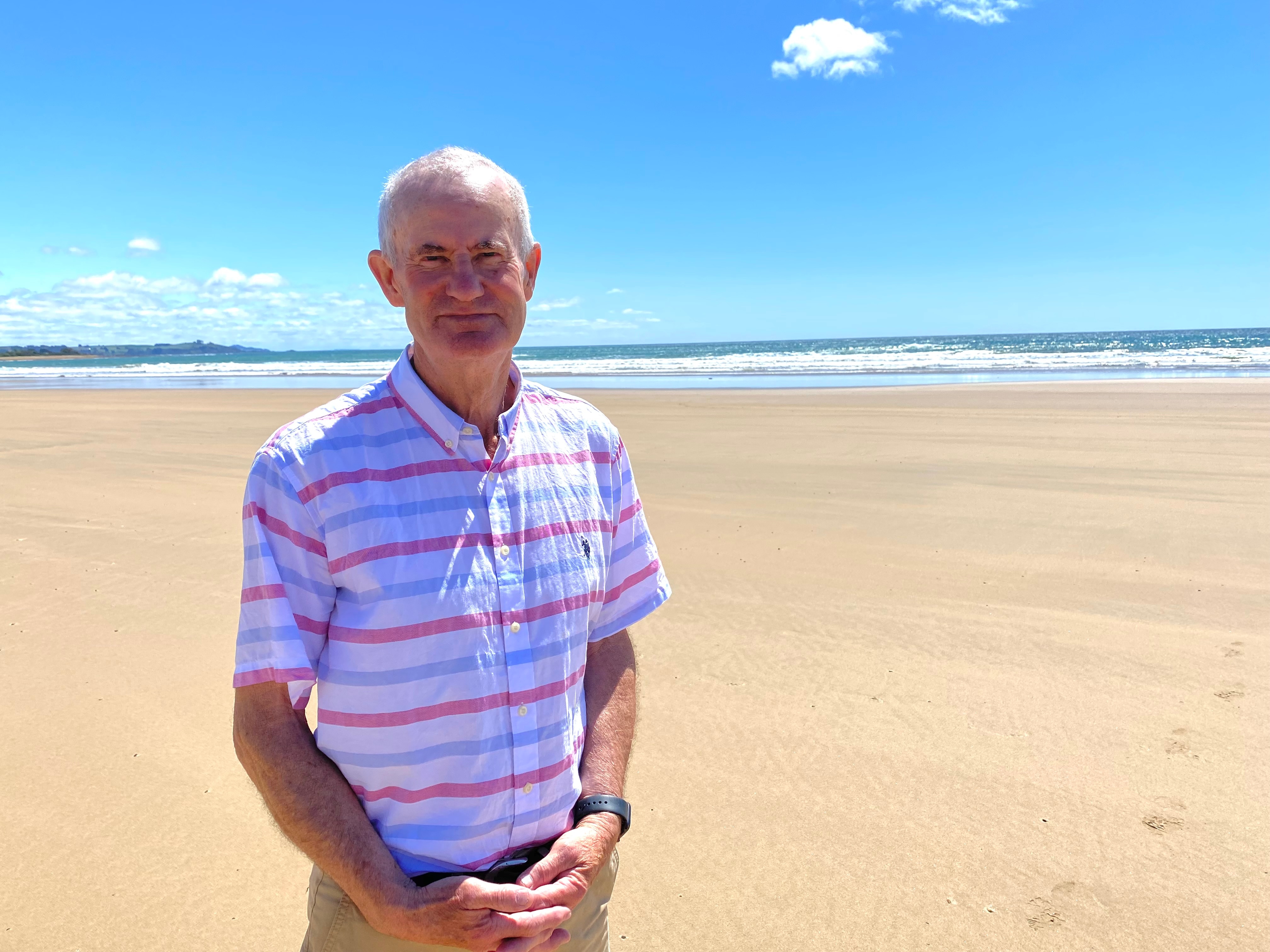 A man wearing a pink striped shirt stands on a beach 