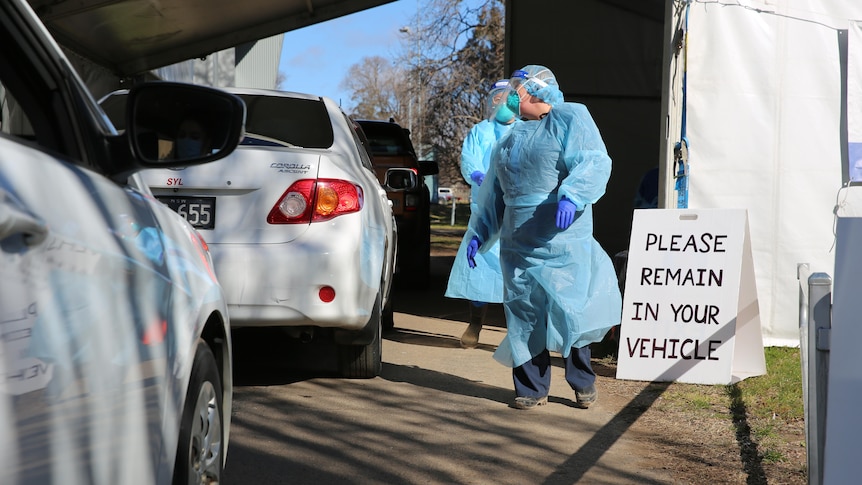 Health official in PPE standing next a line of cars at a COVID-19 testing clinic