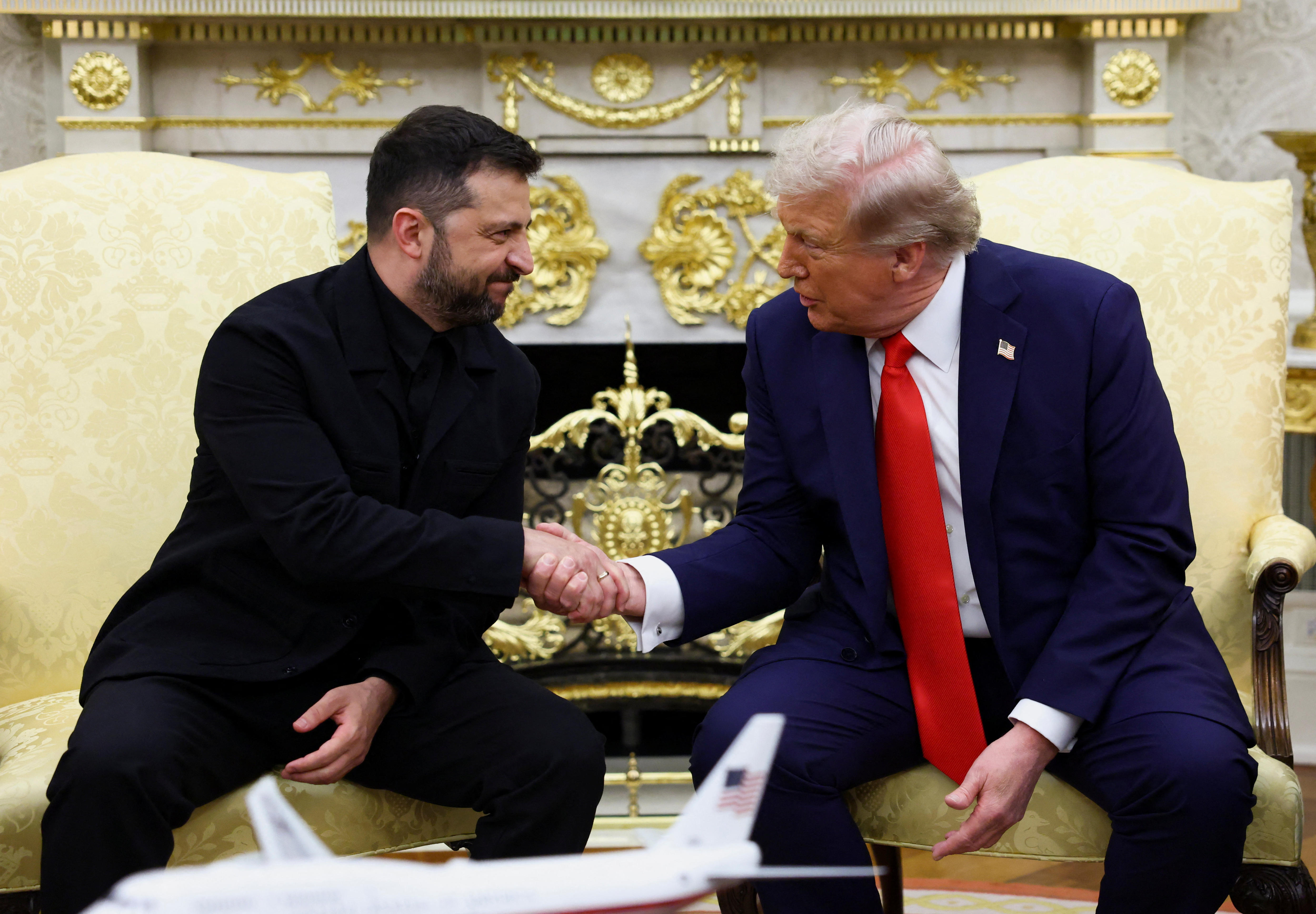Donald Trump and Volodymyr Zelenskyy shake hands while seated in the Oval Office.