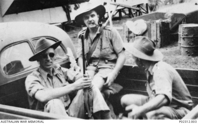 Three men in a black and white photo sit in the back of a truck. 