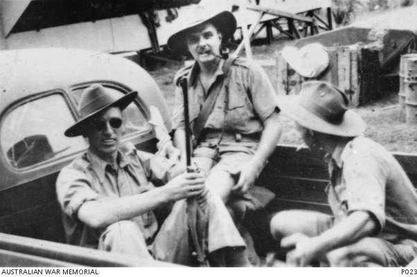 Three men in a black and white photo sit in the back of a truck. 