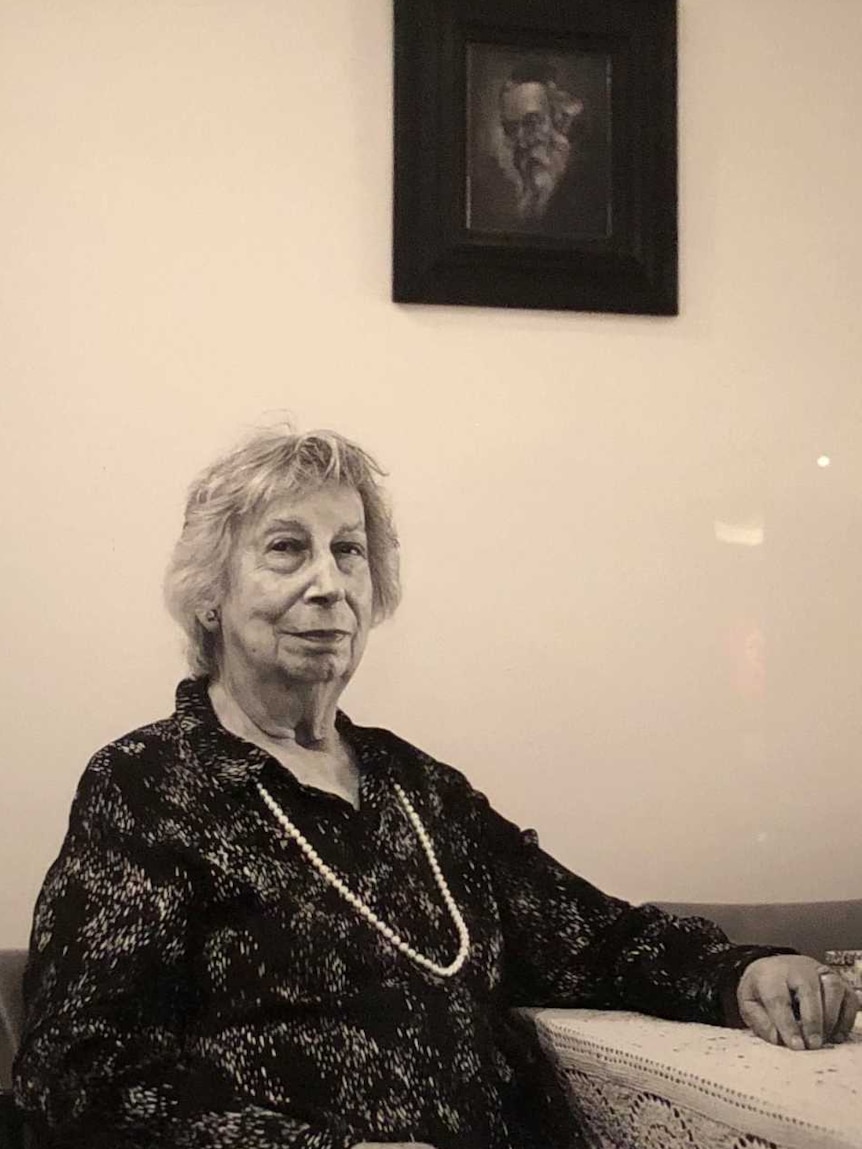 A picture of an elderly woman sitting at her dining room table, hangs in a frame at the Australian War Memorial.