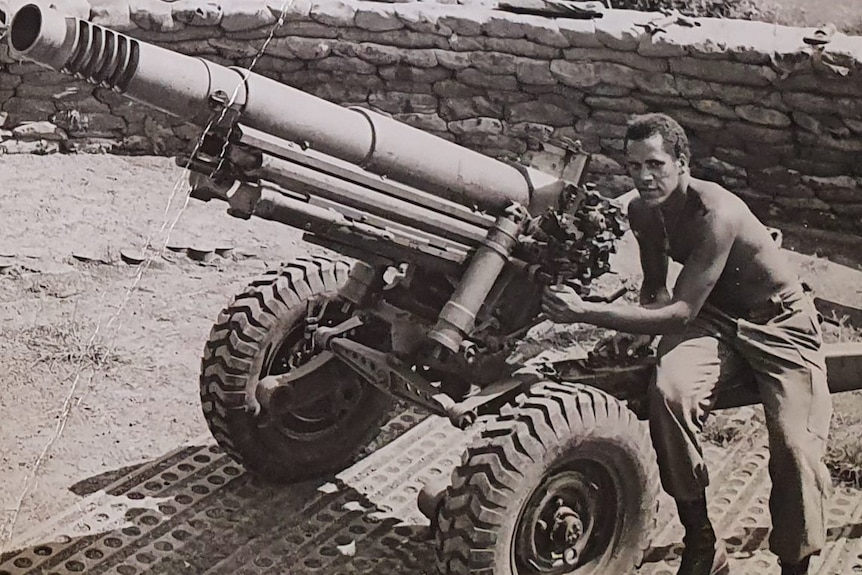 A black and white photo of a man sitting on a gun artillery.