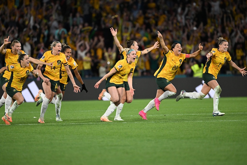 A group of women in yellow soccer shirts celebrate wildly. 