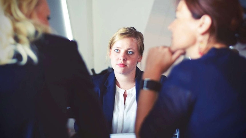 A woman in a suit talks to two other woman across a table in a job interview.