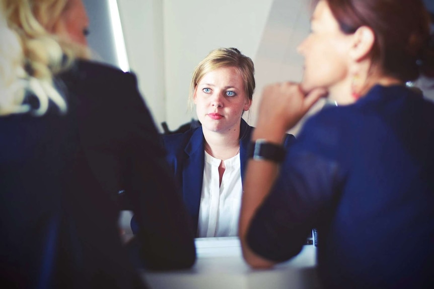 A woman in a suit talks to two other woman across a table in a job interview.