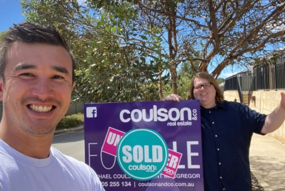 Selfie of a man and a woman with a real estate sold sign