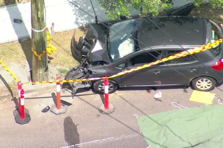 Emergency tape surrounding a pole that a black car has crashed into