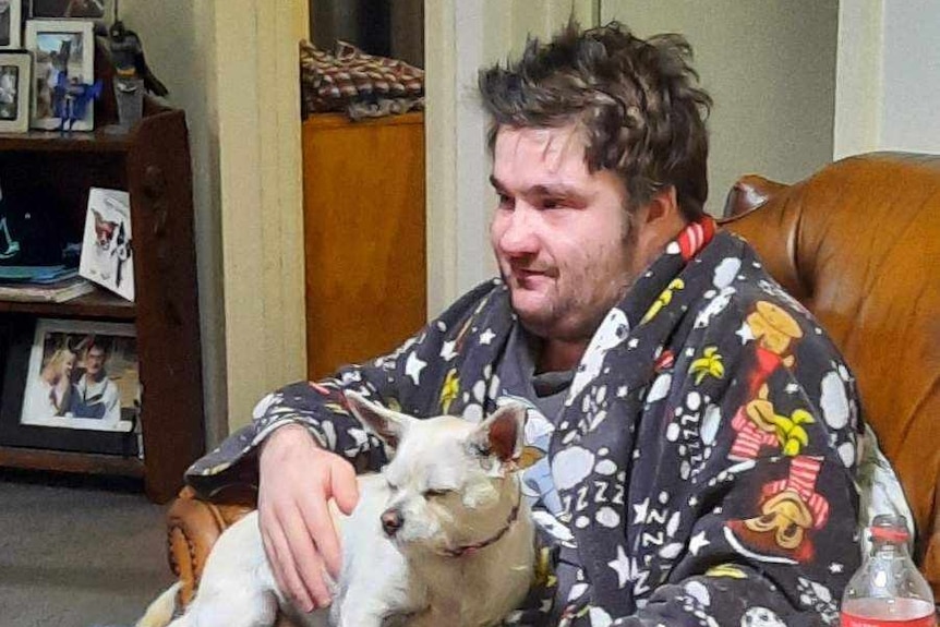 A man sits on a couch with a pet dog on his lap