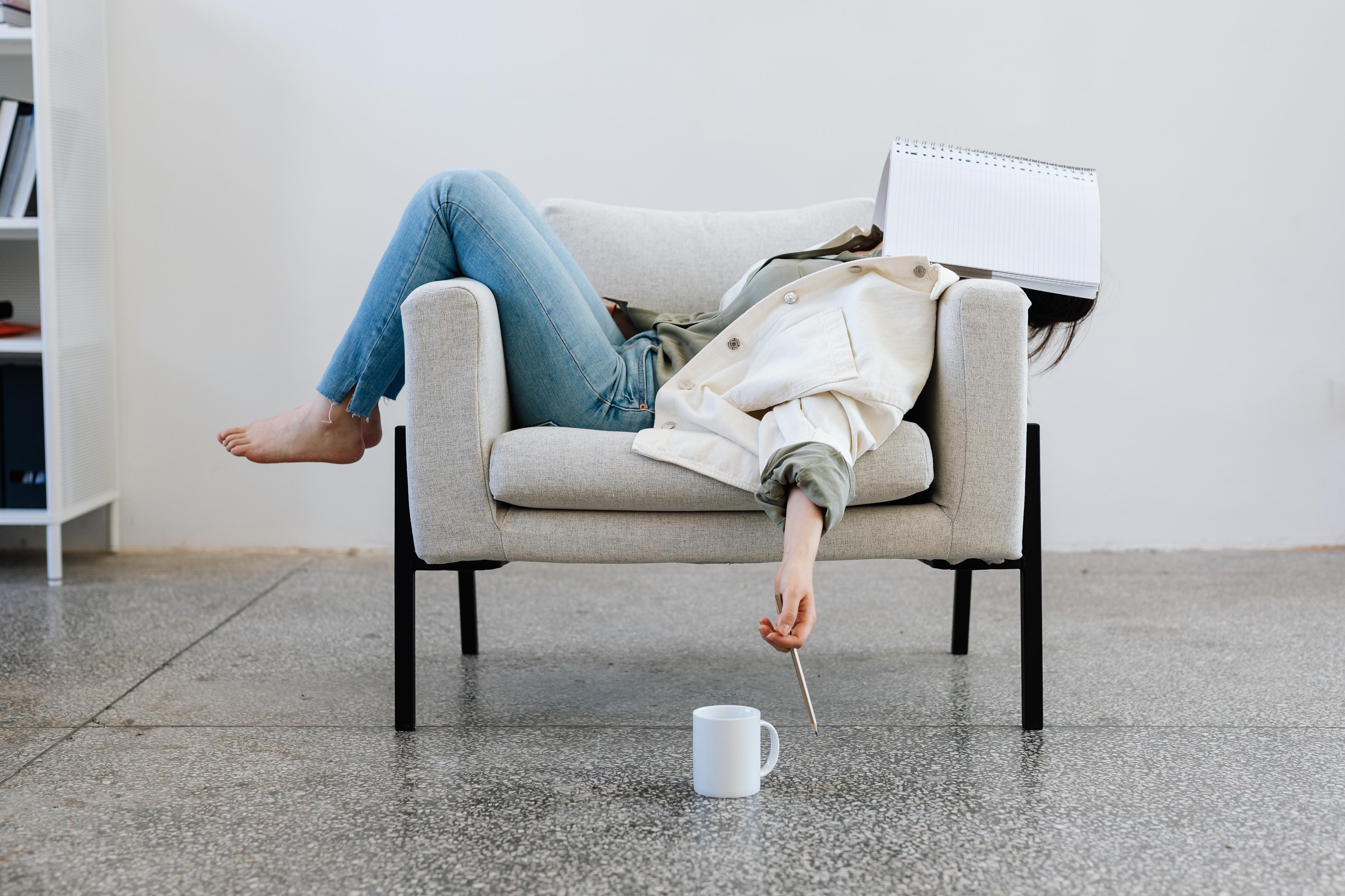 a woman lies across her chair limply with her work notebook across her face