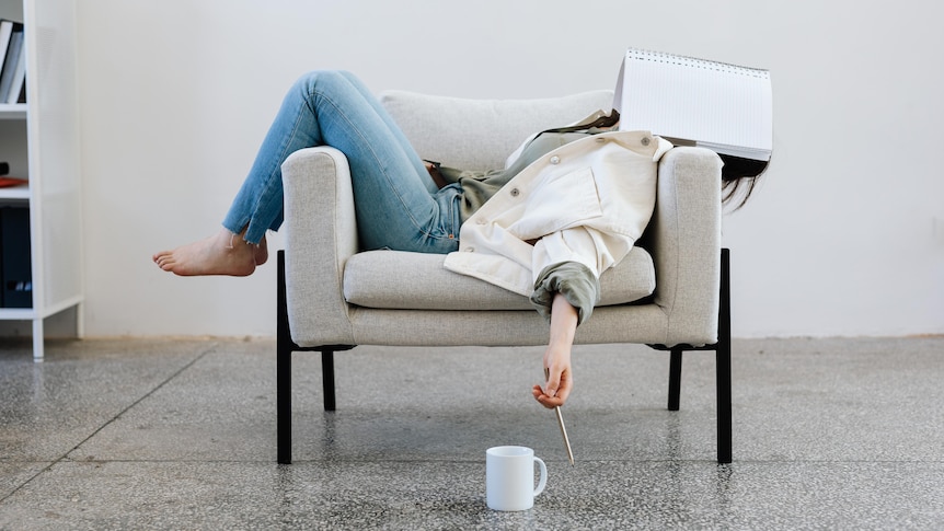 a woman lies across her chair limply with her work notebook across her face