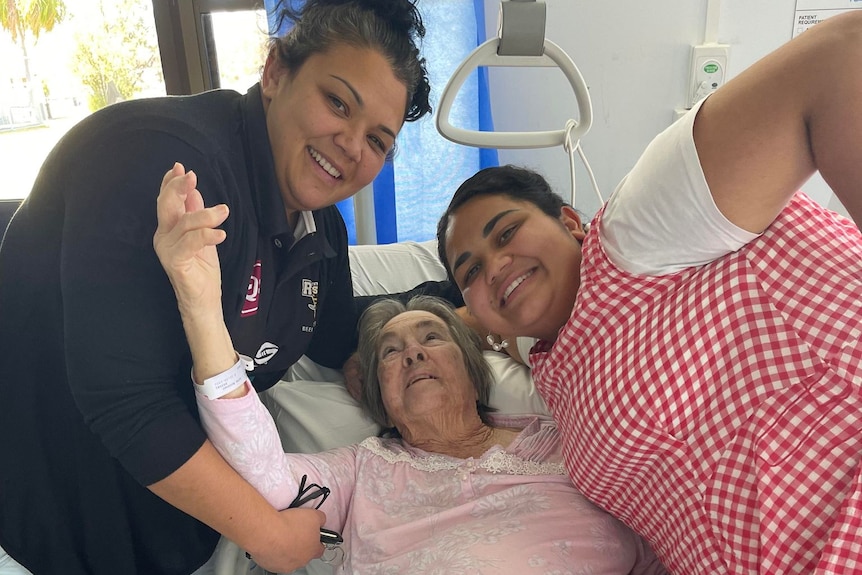 Brianna and Chelsea smiling, on either side of their grandma who is lying in a hospital bed.