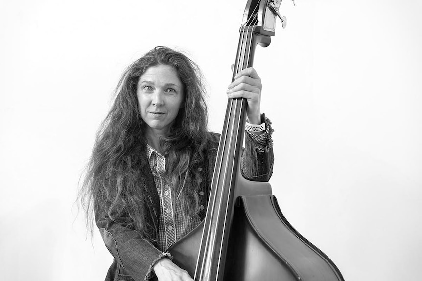 a black and white picture of a woman posing with a large stringed instrument.