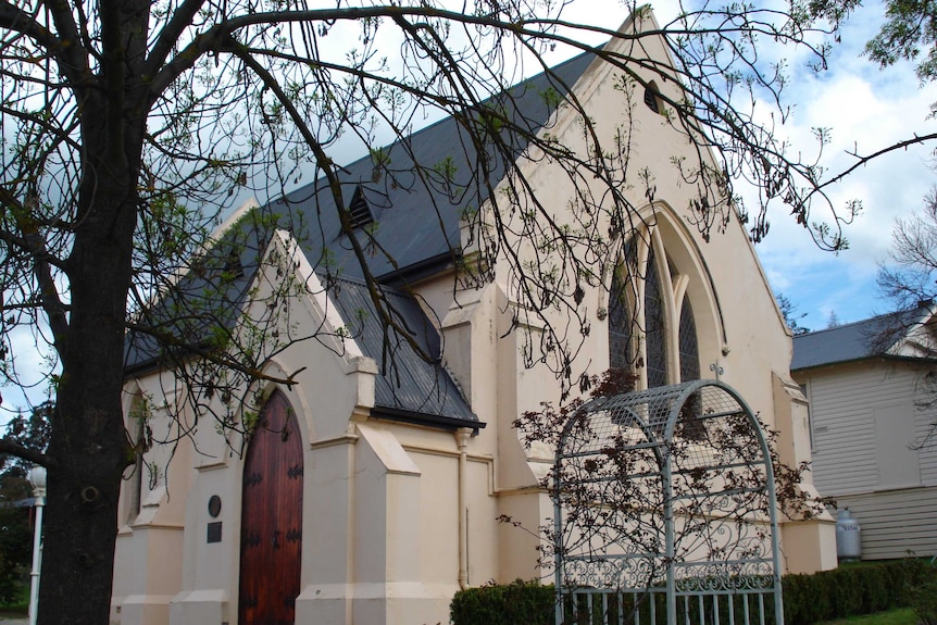 A tree trunk and its branches partly cover St Lukes Anglican Church in Yea