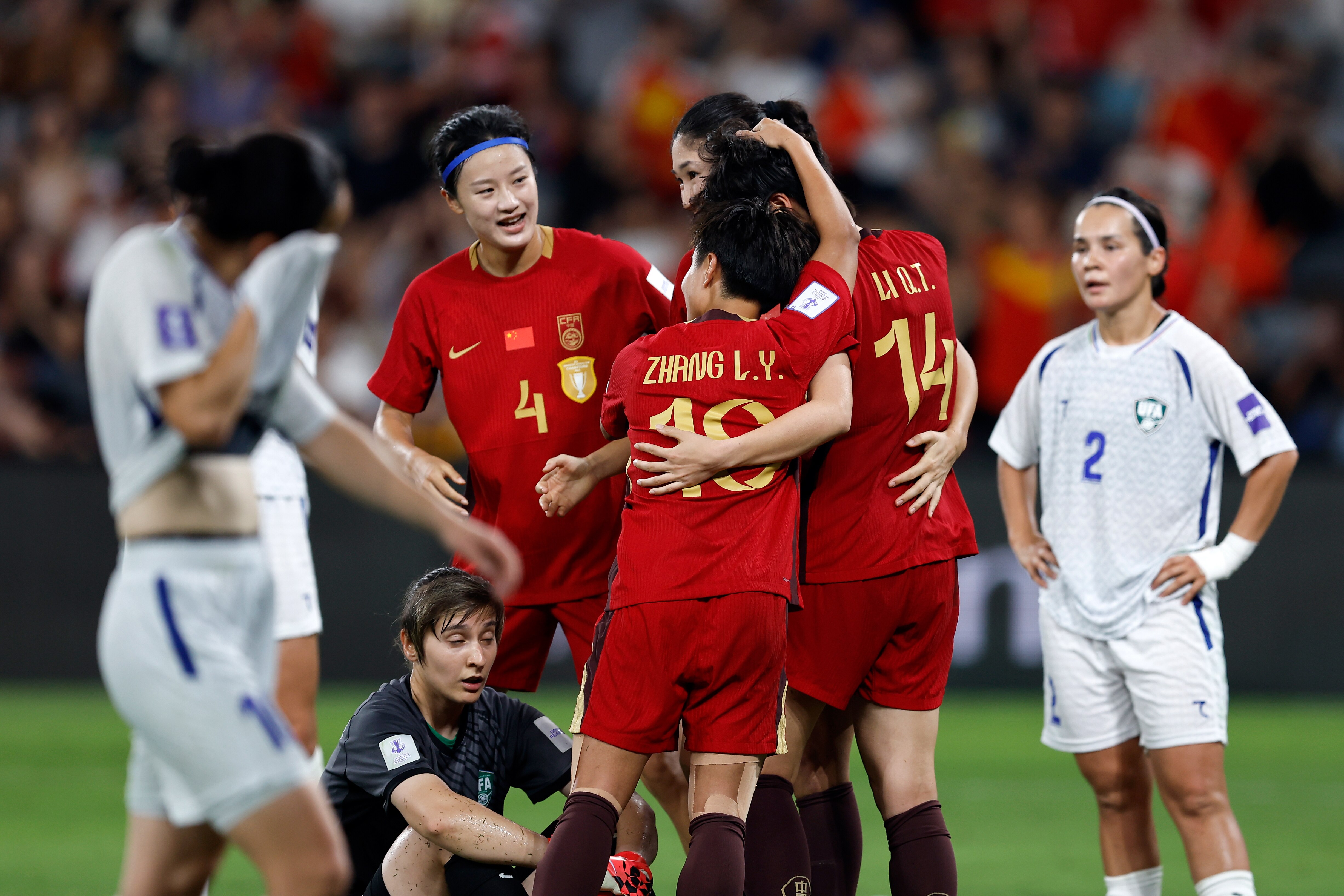 A group of soccer players in red celebrate scoring a goal as players in white look downtrodden