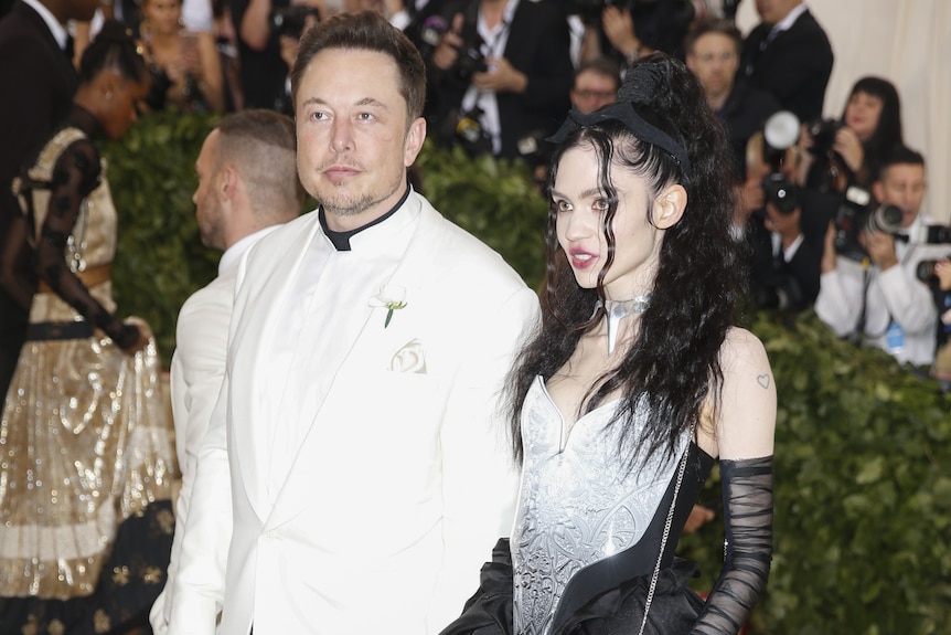 Elon Musk wears a white suit and Grimes wears a metallic dress. 