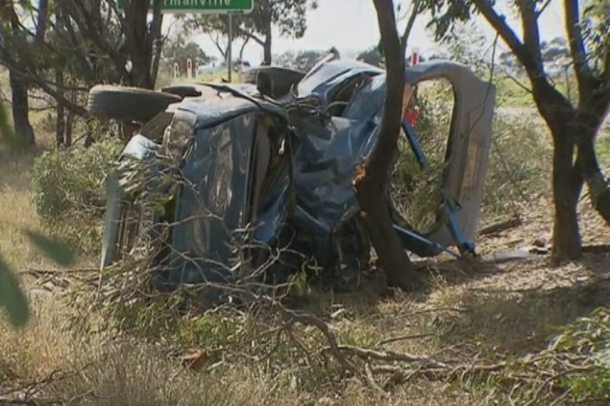 A crumpled blue sedan is seen on the side of the road.