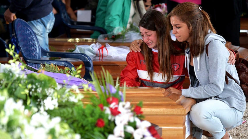 Two women next to the coffin of a relative ahead of a funeral.