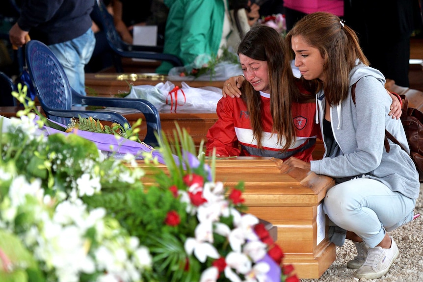 Two women next to the coffin of a relative ahead of a funeral.