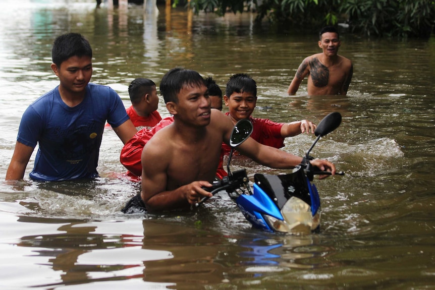 Six men and toys walk and push a motorbike through floodwater