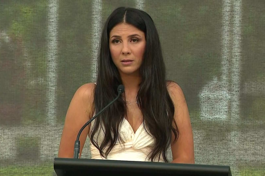 A woman wearing a white dress stands at a lecturn.