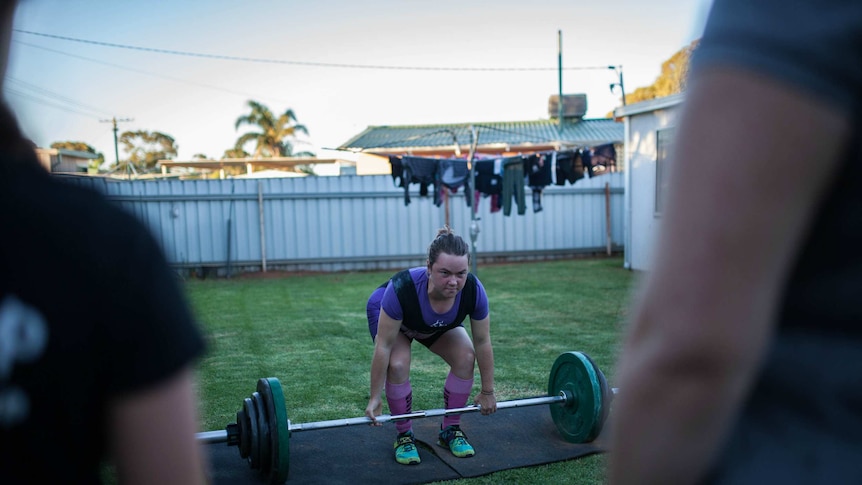 Maddy Keast prepares to demonstrate a powerlift with a barbell in her backyard.