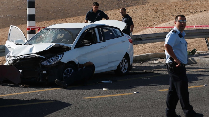 Israeli security forces stand around a crashed car.