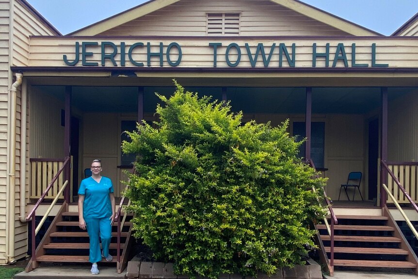 Topaz Stringfellow wears blue scrubs while standing in front of Jericho Town Hall 