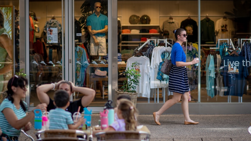 A woman walking past a group sitting at a table in the Smith St Mall, in the Darwin CBD.