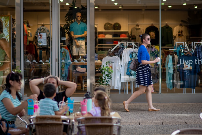 A woman walking past a group sitting at a table in the Smith St Mall, in the Darwin CBD.