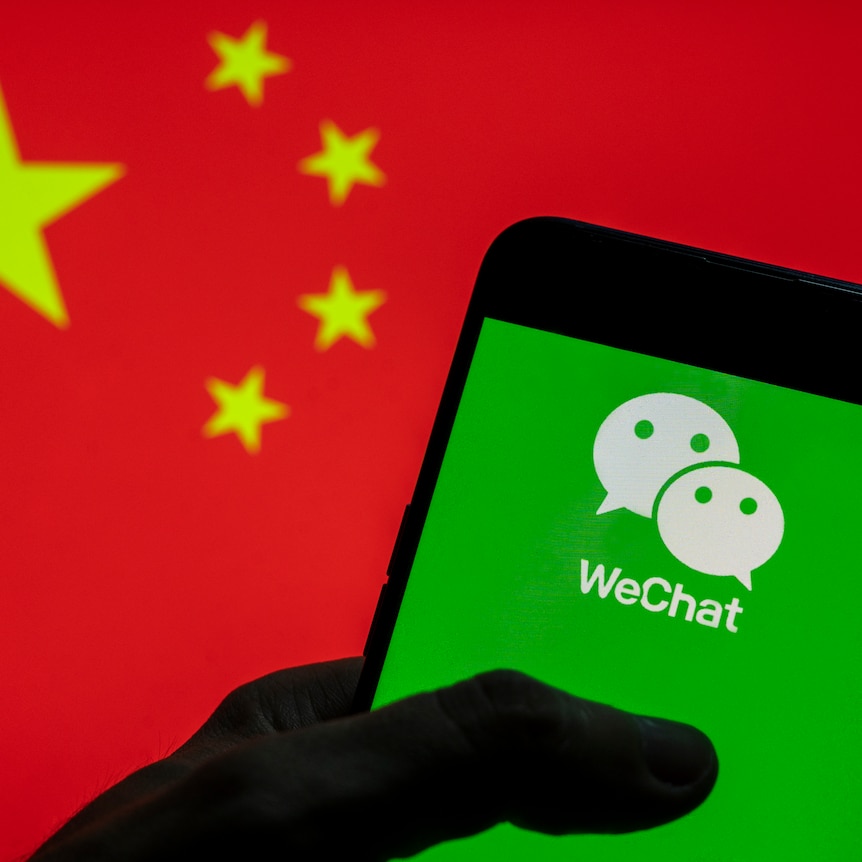 Bright green WeChat logo (2 white faces on green background) held by shadowed hand, bright red Chinese flag background