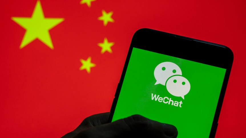 Bright green WeChat logo (2 white faces on green background) held by shadowed hand, bright red Chinese flag background
