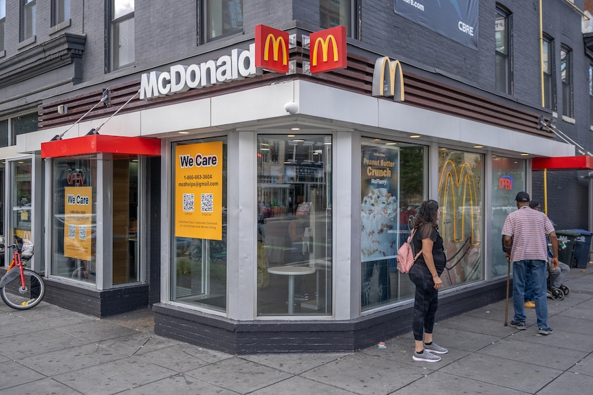 A McDonalds store in a corner building, with several people gathered outside.