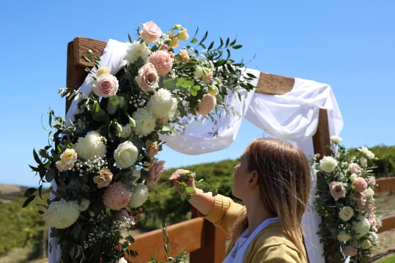A woman putting floral arrangements on a wooden frame for a wedding.