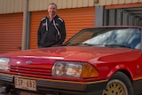 A man standing next to a red 1982 Ford Falcon XE ESP.