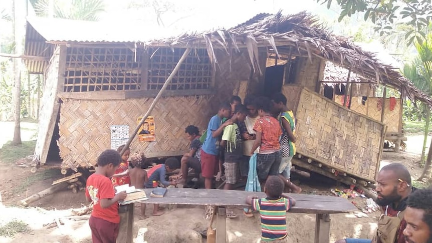 children stand around a thatched house that has been affected by the quake.