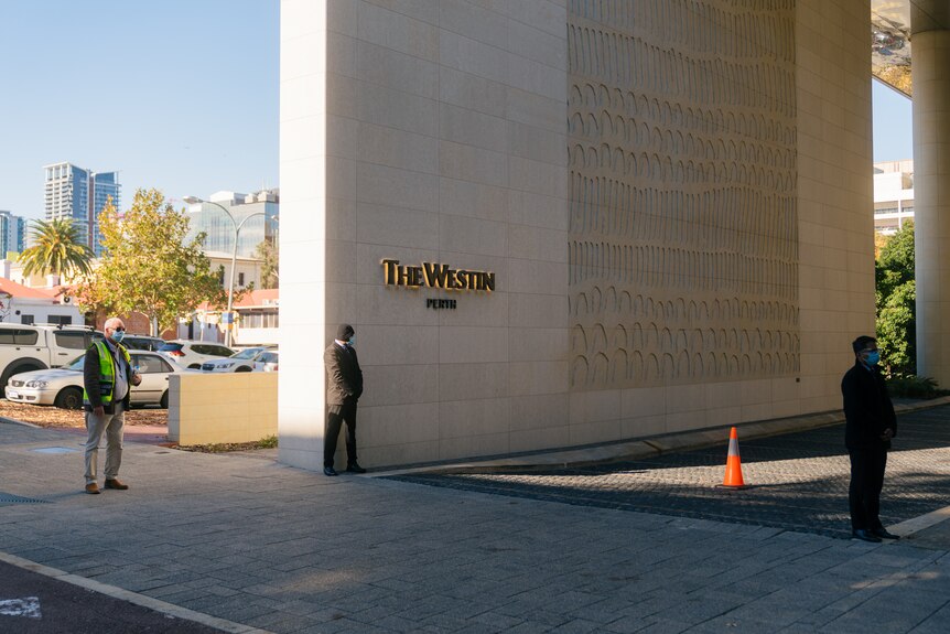 The entry to a hotel on a sunny day, with two security guards out the front, and a sign on a big wall that reads "The Westin"