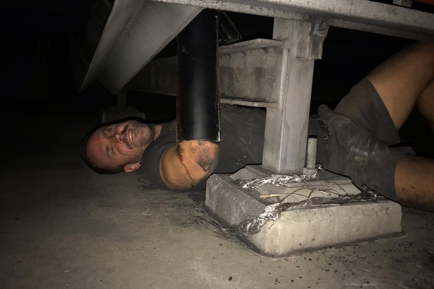 A man lying under a conveyor belt at a coal port.